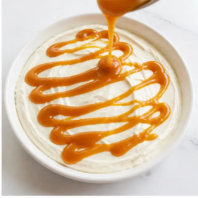 Step 2: Drizzle the golden caramel sauce evenly across the top of the cheesecake layer, letting it pool into glossy ribbons and swirls.
