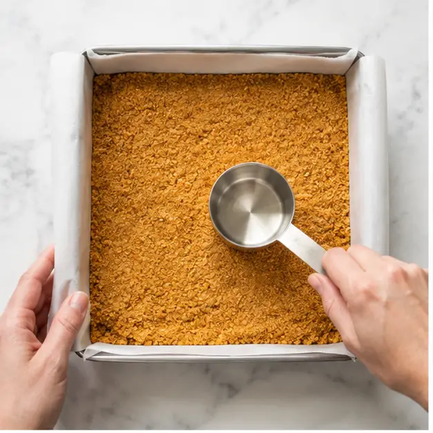 Step 1: Pressing the buttery graham cracker crust into the baking pan