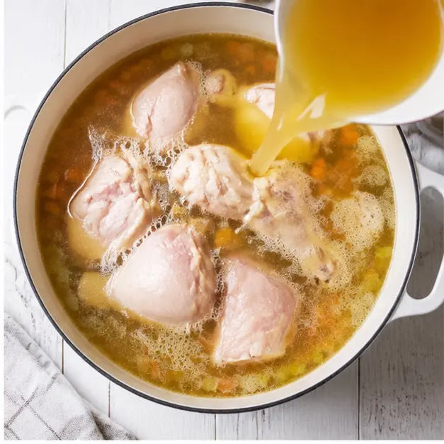 Adding raw bone-in chicken pieces and golden broth to the pot for simmering